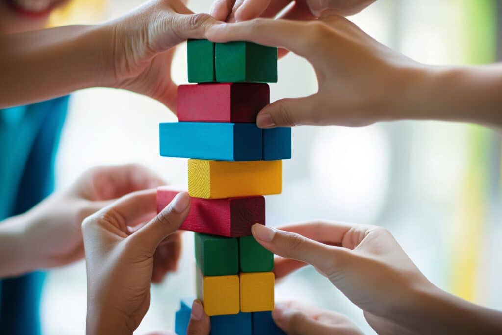 De nombreuses mains construisent ensemble une haute tour avec des blocs en bois colorés : verts, rouges, bleus et jaunes. Symbole de collaboration et d'unité.